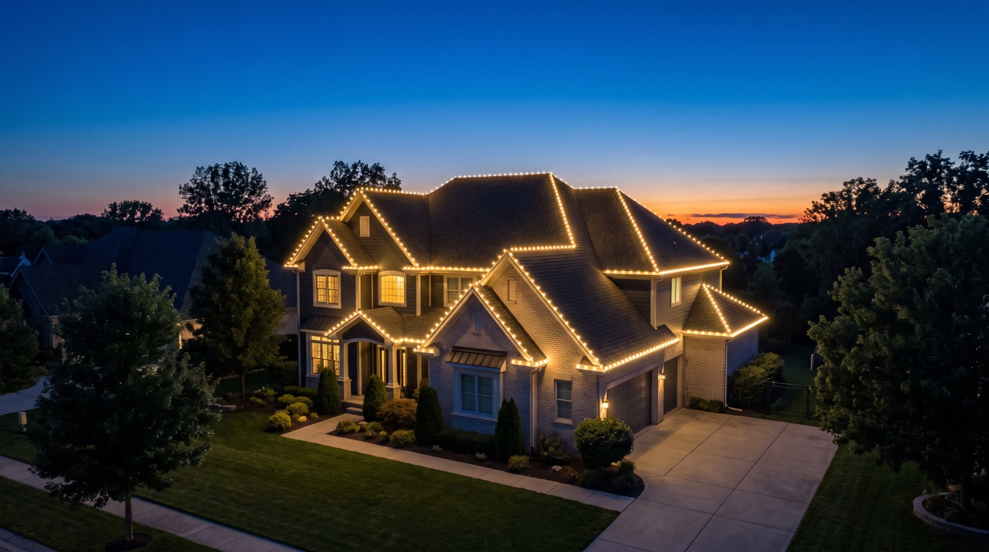 Aerial three-quarter view of a two-story home at dusk, roofline traced in warm white lights